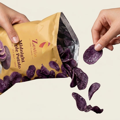 Hand holding a Midnight Purple Potato chip beside the open pack