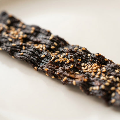 Close-up of a Smoke and Sesame Shiitake Jerky strip, slow-smoked and finished with toasted sesame seeds